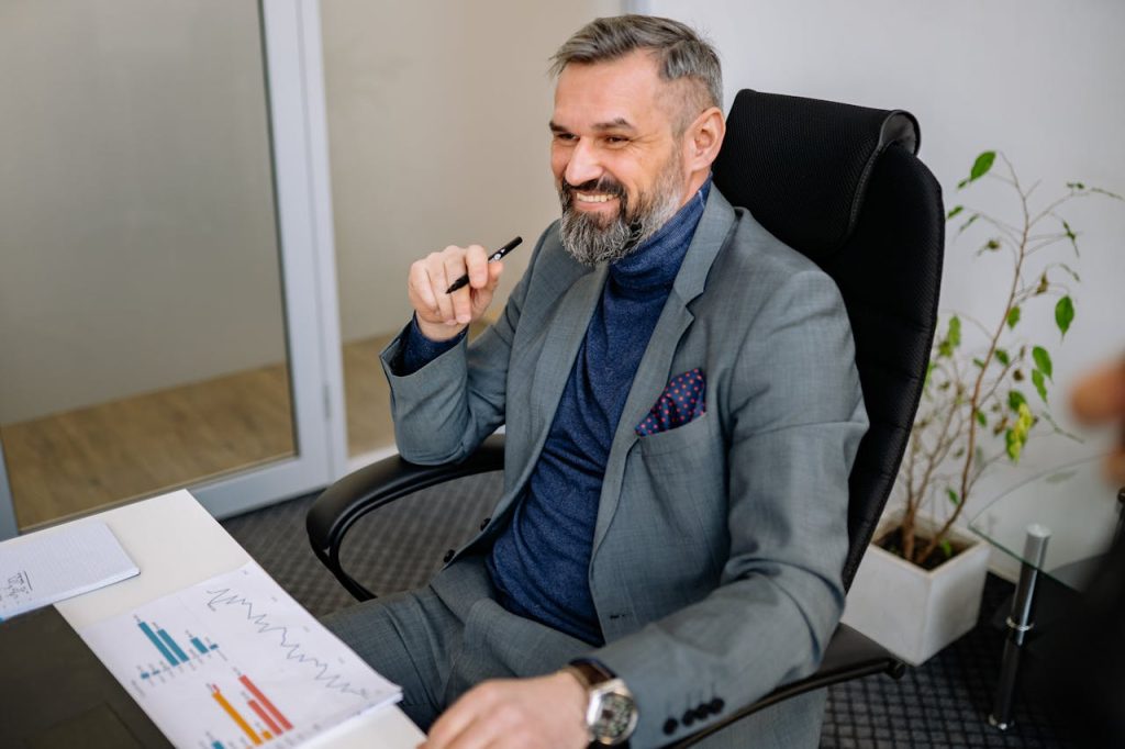 Smiling businessman in a suit sits at a desk, illustrating office professionalism.